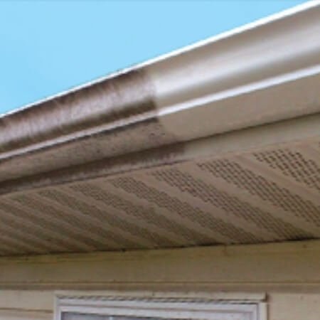 A length of house guttering, dark with staining on the left and brightened back to white on the right